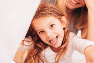 Portrait of a little baby girl smiling to the camera showing her tongue, her mom is smiling in the background