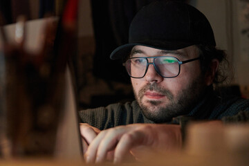 A close-up shot of a man using a laptop in a dimly lit room, engrossed in his digital work during...