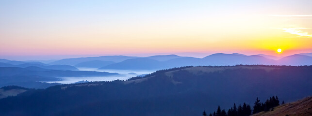 Colorful clouds in the sky at sunset against the backdrop of a mountainous forest area.