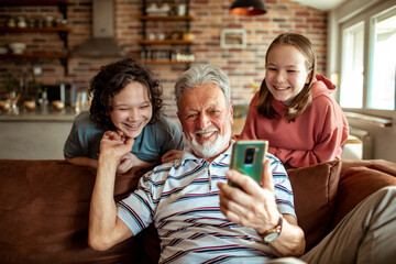 Grandfather using the smartphone with his grandchildren on the couch at home