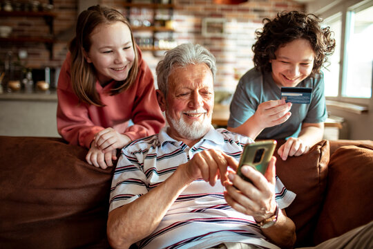 Grandfather and grandchildren online shopping from a smartphone on the couch at home