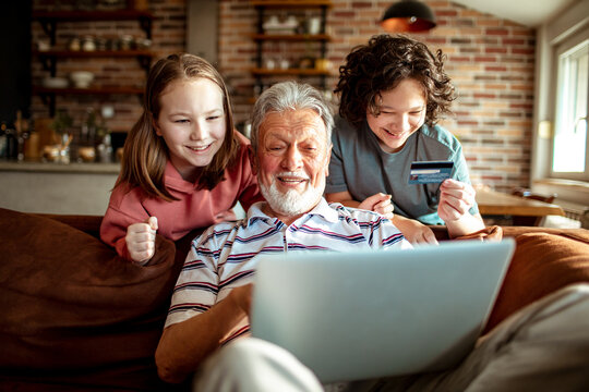 Grandfather and grandchildren online shopping from a laptop on the couch at home