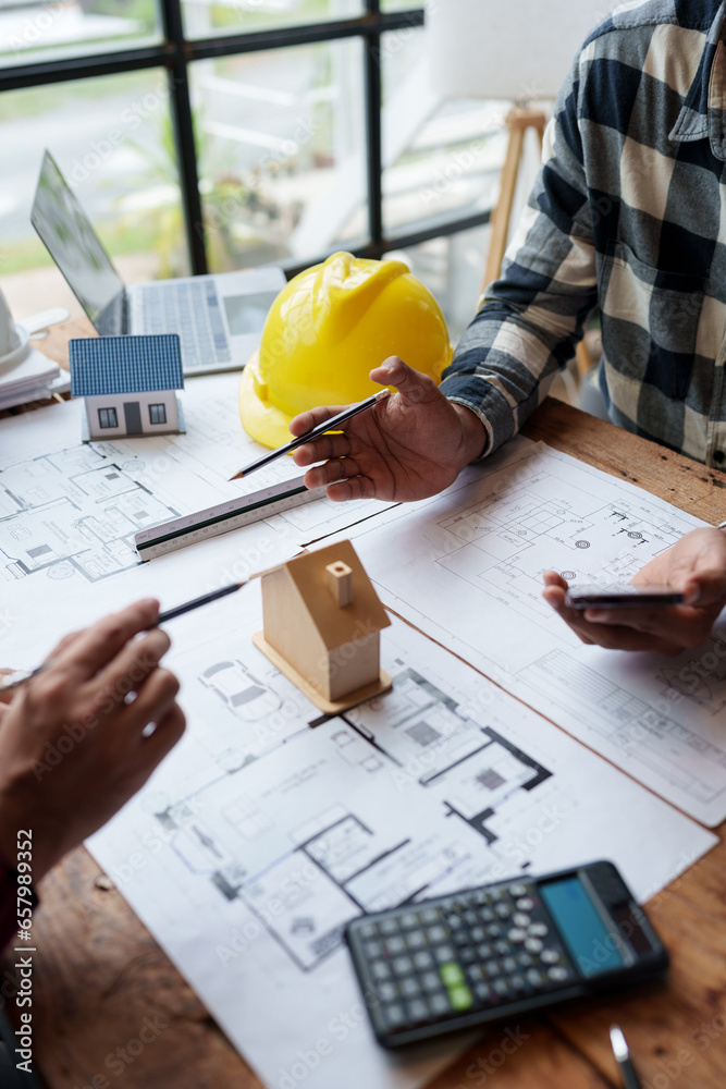 Wall mural Two young Asian businessmen or architects are describing architectural house model in their office together for the construction of housing estate project in prime location the location is perfect