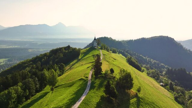 View from above of the serene beauty of the small Church of St. Primoz in Jamnik at sunrise on a green hill in Slovenia, Kranj, Gorenjska