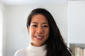 Headshot of young smiling asian woman looking at camera indoors.