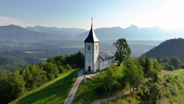 View from above of the serene beauty of the small Church of St. Primoz in Jamnik at sunrise on a green hill in Slovenia, Kranj, Gorenjska