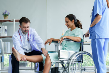 Male orthopedic doctor lifting the leg of a Spanish female patient in a wheelchair. Lift your leg up and down to check for injuries. To prepare for physical therapy with a physical therapist.