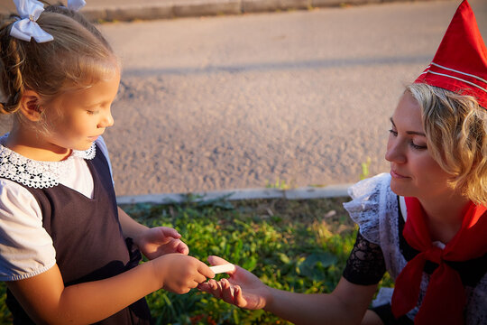 Young and adult schoolgirl on September 1 drawing by chalk on asphalt. Generation of schoolchildren of USSR and Russia. Female pioneer in red tie and October girl in modern uniform. Mom and daughter