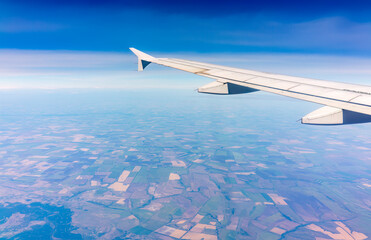 Obraz premium Aerial view from airplane window above green ground. View from the airplane window with beautiful clouds at sunrise