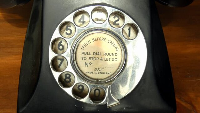 A close of up an old vintage rotary dial telephone. A hand demonstrates how its used by turning the dial with the finger.