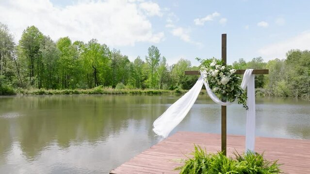 Religious cross with clothe draped across blowing in the wind on the dock of a lake.
