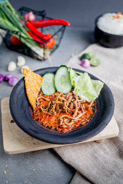 Sambal gami usus ayam or 
chicken intestine with sambal cooked in earthenware plate against wooden background. Served on wooden table