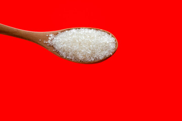 Wooden spoon with sugar crystals on red background