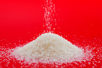 Pile of white sugar crystals on red background