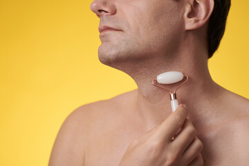 Cropped image of mature man massaging neck with rose quartz roller, isolated on yellow