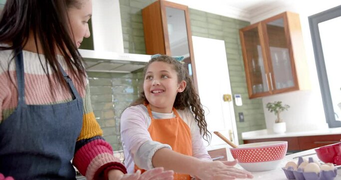 Happy biracial mother and daughter putting dough into cake tin and smiling in sunny kitchen