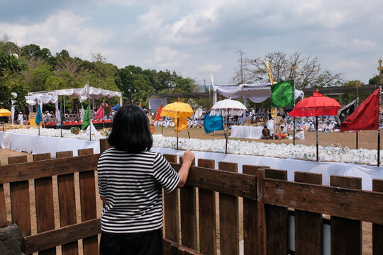 A woman standing behind a wooden fence is watching a religious ceremony
