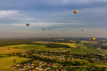 Many hot air balloons over a field, forest, village against the background of Cumulostratus clouds. Aerial view. Multi-colored balloons that look like a rainbow.