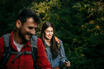 A committed couple in full hiking attire and backpacks, deep in conversation as they explore a pristine mountain forest together