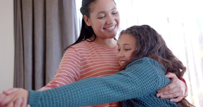 Happy biracial mother and daughter dancing and embracing in sunny bedroom