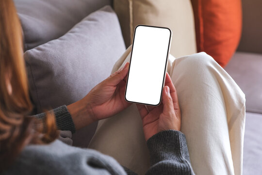 Mockup image of a woman holding mobile phone with blank desktop white screen while lying on a sofa at home
