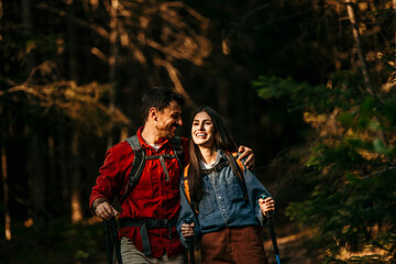 Two nature enthusiasts, a Latina woman, and her Caucasian partner, trek through the serene mountain forest while geared up for an exciting hike.
