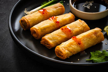 Vegetable filled spring rolls and soy sauce on black wooden table
