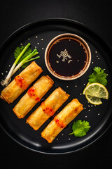 Vegetable filled spring rolls and soy sauce on black wooden table
