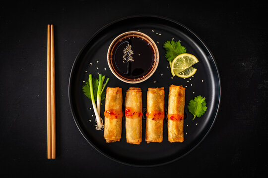 Vegetable filled spring rolls and soy sauce on black wooden table
