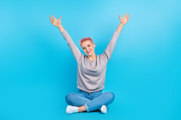 Fototapeta na wymiar Full length photo of overjoyed cheerful person sit floor crossed legs raise arms isolated on blue color background