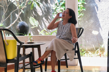 An Asian woman sitting on a wooden chair while talking on the phone