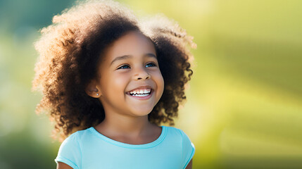 Close-up of a smiling little girl with white perfect teeth, against a green nature background with copy space. Children's Dental Care. Dentistry concept.