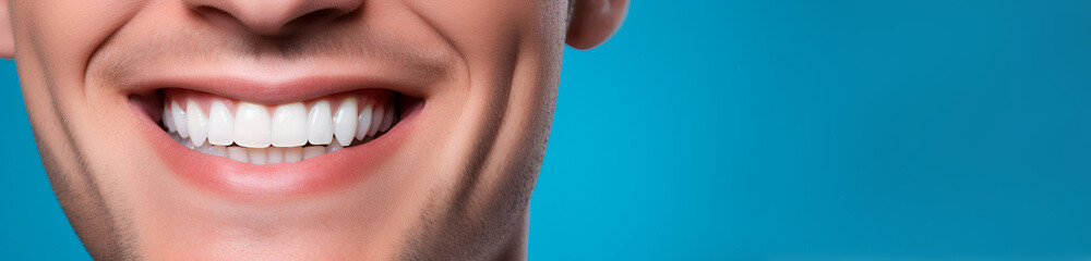 Banner Close-up of a smiling young man with a beard and white perfect teeth, isolated on a blue studio background with copy space. Dental care. Stomatology. Dentistry concept.