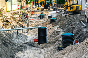 Street reconstruction view with a wide trench, replaced sewer and water pipes and inspection wells - obrazy, fototapety, plakaty