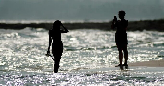 Silhouette of women taking pictures near the sea. The meanders of the ocean crash against the shore. happy people on vacation. High quality 4k footage