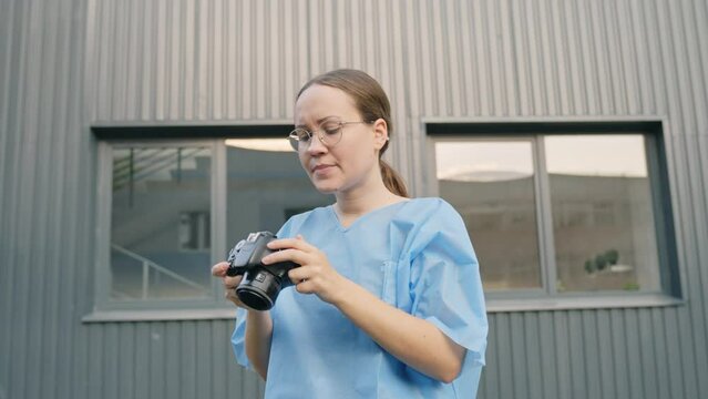 Woman Photographing a Crime Scene Investigation Wearing a Blue Protective Outfit. Outside Mid Shot with Perspective Looking Up at Person with Building in the Background. 