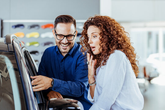 Cute couple peering into a car at a dealer while deciding whether to buy. Young couple buying new car. It is the one car I want! Beautiful young couple standing at the dealership