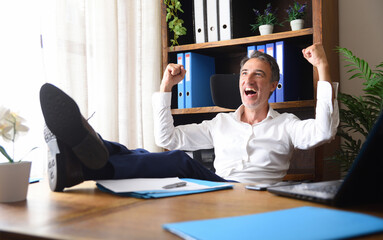 Euphoric businessman celebrating work success with feet on the table