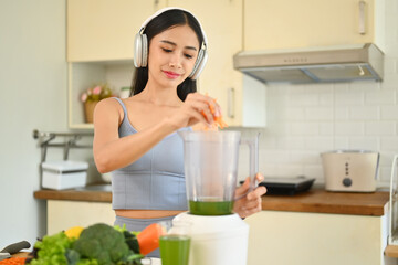 Obraz na płótnie Canvas Happy young woman making healthy green smoothie with blender in kitchen. Healthy lifestyle concept