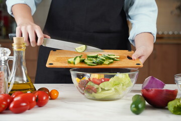 The woman in the process of making vegetable salad. Closeup of hands  cutting cucumber on wooden cutting board