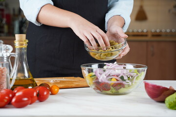The Girl adds olives to salad of fresh vegetables. The Girl in the process of making vegetable salad.