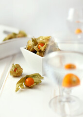 Physalis in white bowl on wooden table on background of water glass. Autumn still life.