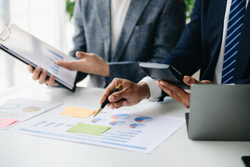 Business documents on office table with smart phone and laptop and two colleagues discussing data in the background