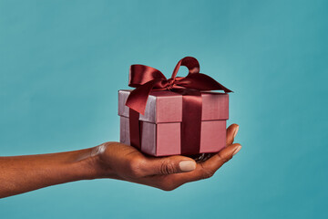 Black female hand holding gift box on blue