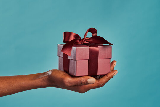 Black female hand holding gift box on blue