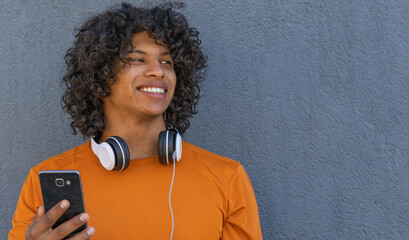 young attractive latin man in an urban style with headphones and smartphone - obrazy, fototapety, plakaty