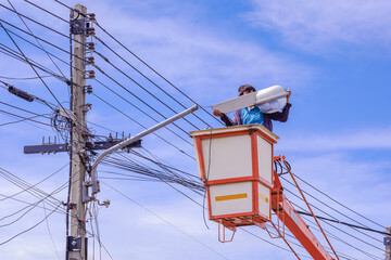Electrician in bucket boom truck is repairing street light pole against blue sky background © Prapat