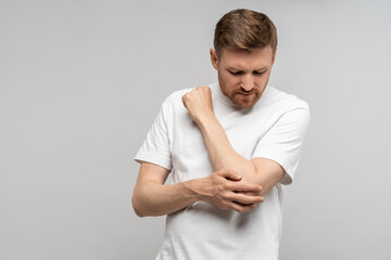 Man touching hand elbow feeling pain isolated on gray background after injury. Neuralgia, pinched nerve in arm after injury, broken fracture bruised hand. Health problems, bad symptom, hurt concept. - obrazy, fototapety, plakaty