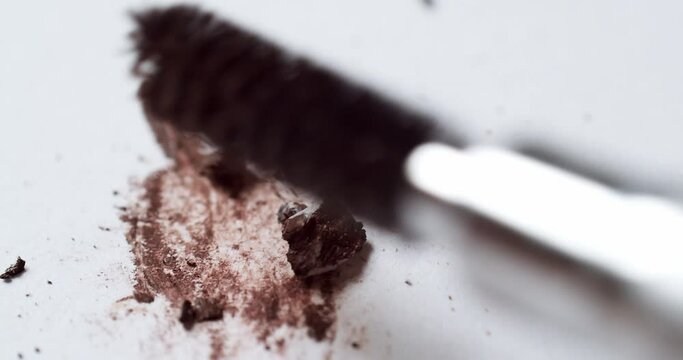 Blending a dark-brown toned mascara loose powder using an eyelash wand applicator on a blank white board.