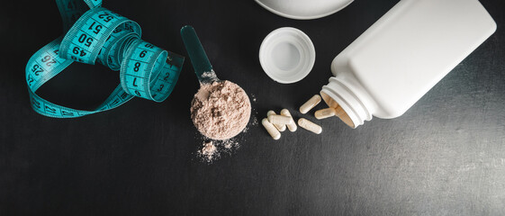 Chocolate whey protein powder in measuring spoon, white capsules of amino acids, vitamins and...